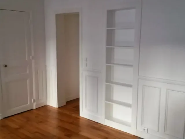 Rénovation intérieure : pièce vide avec parquet bois, moulures murales blanches et porte à panneaux – menuiserie et peinture.